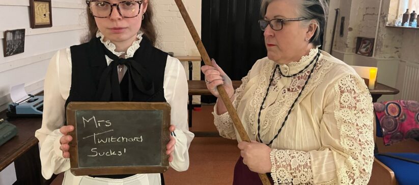Two women in period clothing holding a chalkboard